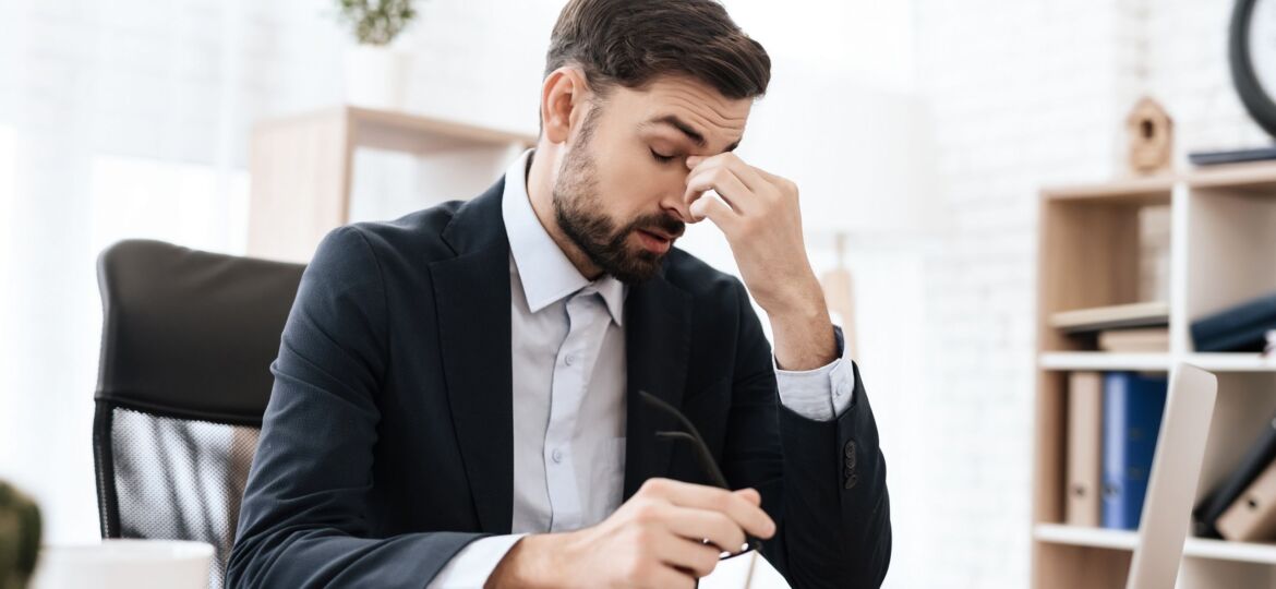 Man in the office is sitting and holding his head in pain.